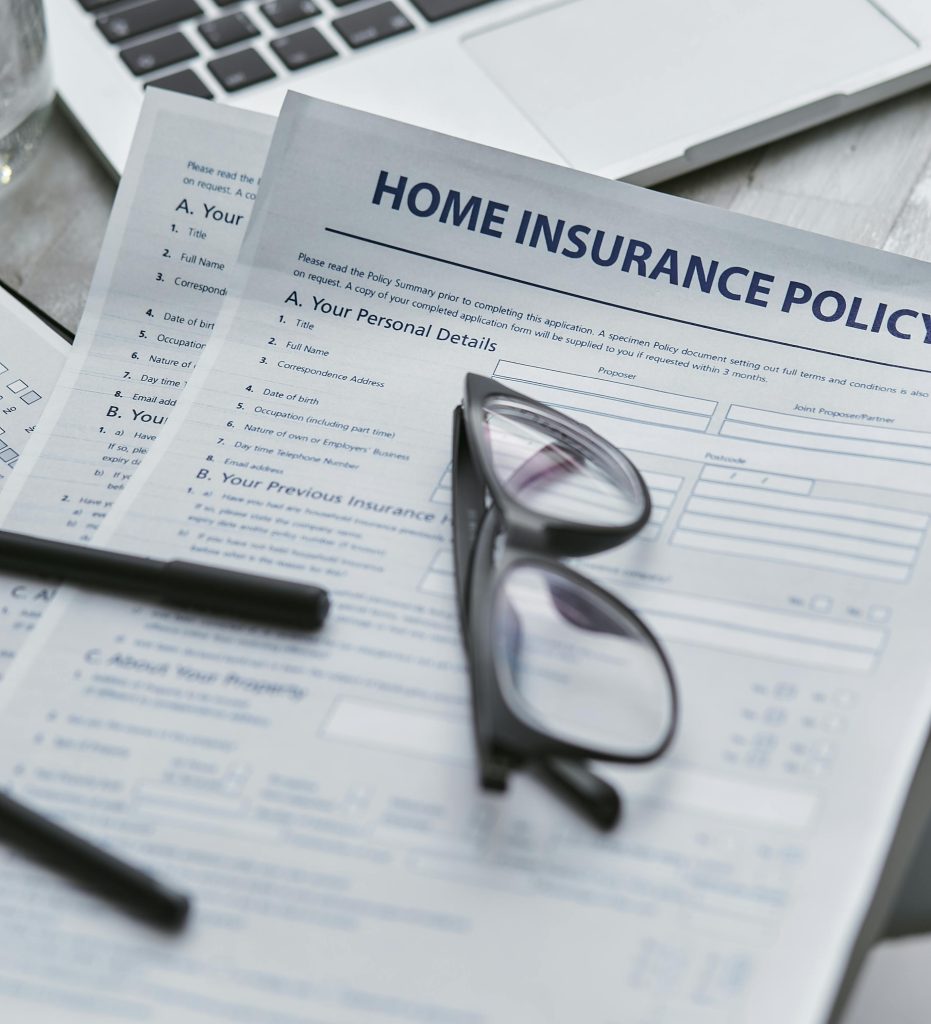 A pair of eyeglasses resting on top of a home insurance policy form, with a pen nearby on a table.